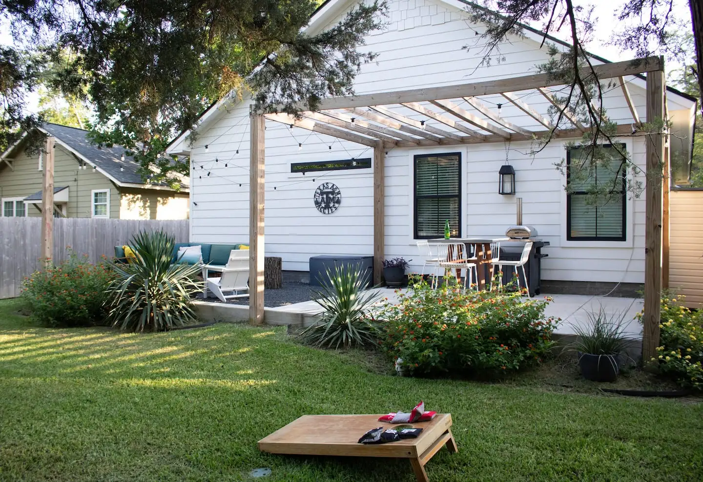 Fenced backyard with pergola, patio dining, and cornhole